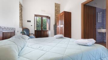 A bedroom with a large bed, a chair, a wooden wardrobe, and a bathroom visible through an open door.