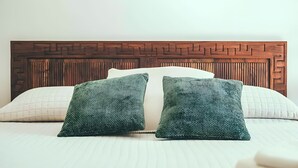 Una cama con cabecera de madera, dos almohadas estampadas y una almohada blanca lisa.