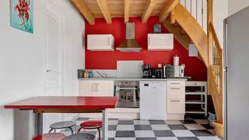 A kitchen with a red wall, white cabinets, a wooden ceiling, and a checkered floor.