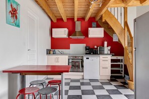A kitchen with a red wall, white cabinets, a wooden ceiling, and a checkered floor.