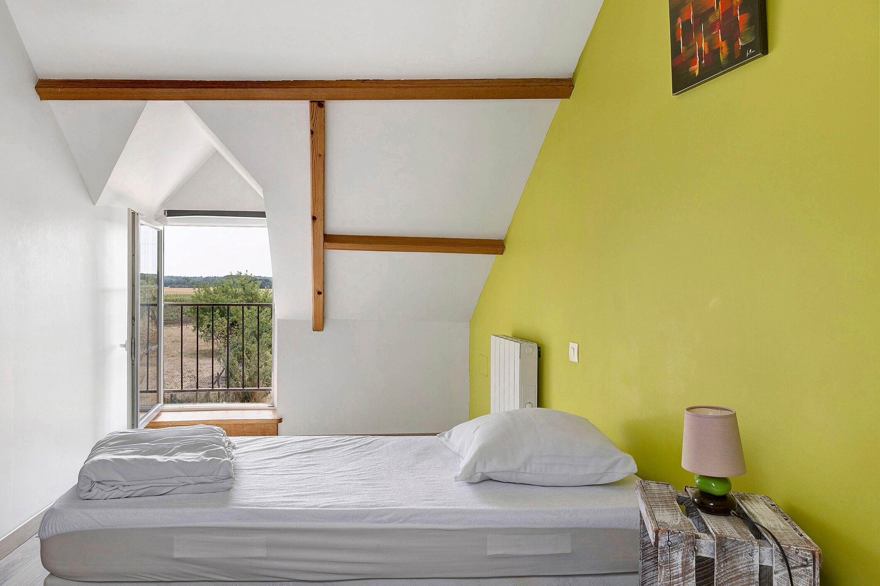 Ein Schlafzimmer mit einem Bett, einem Nachttisch, einer Lampe und Blick durch ein Fenster.