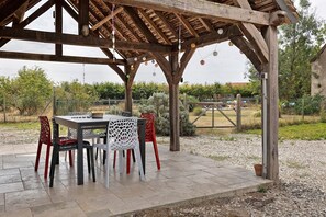 A covered outdoor dining area with a table and chairs, surrounded by a fence and greenery. - Charming Country House with Shared Pool and Wi-Fi (Selles-sur-Cher)