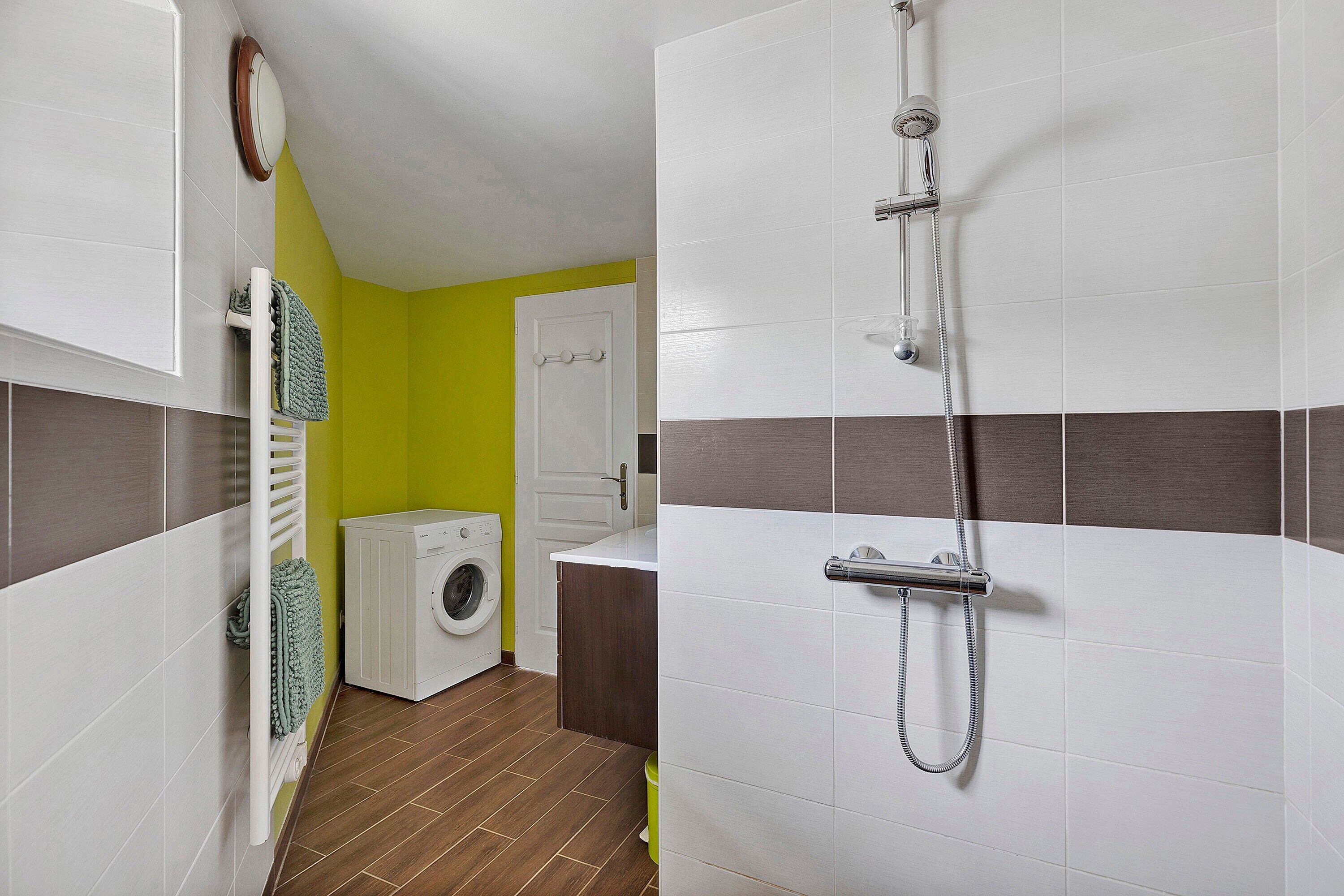 A compact bathroom with a washing machine, a shower, and a toilet.