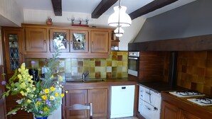 Una cocina con armarios de madera, salpicadero de azulejos, horno empotrado y un jarrón azul con flores sobre la mesa.