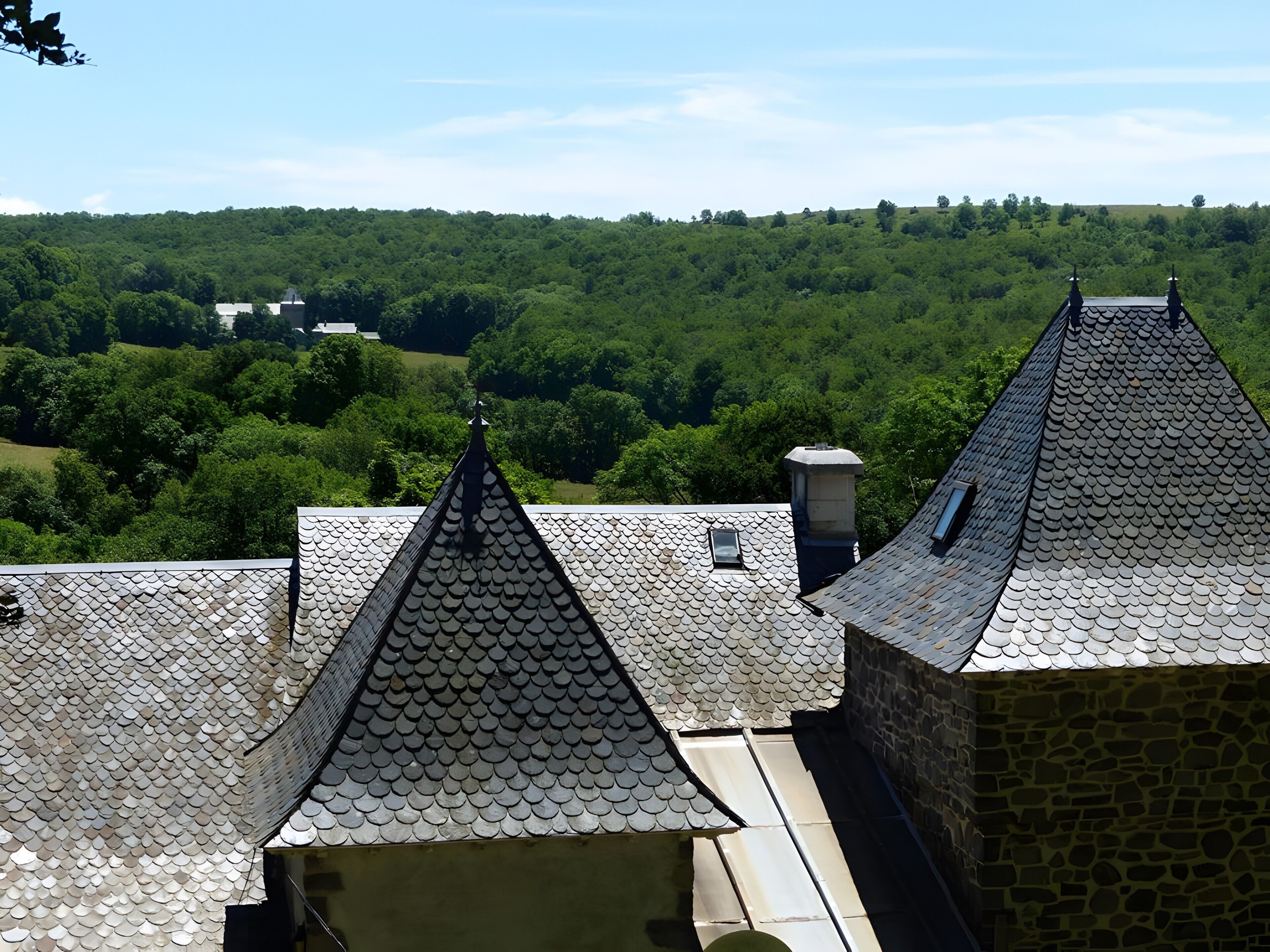 A building with multiple roofs, one with a pointed peak and another with a rounded top, surrounded by lush green hills.