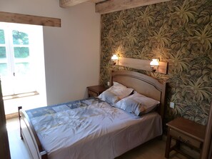 Ein Schlafzimmer mit einem Bett, zwei Nachttischen, einem Fenster und einer Wand mit einem Blumenmuster.