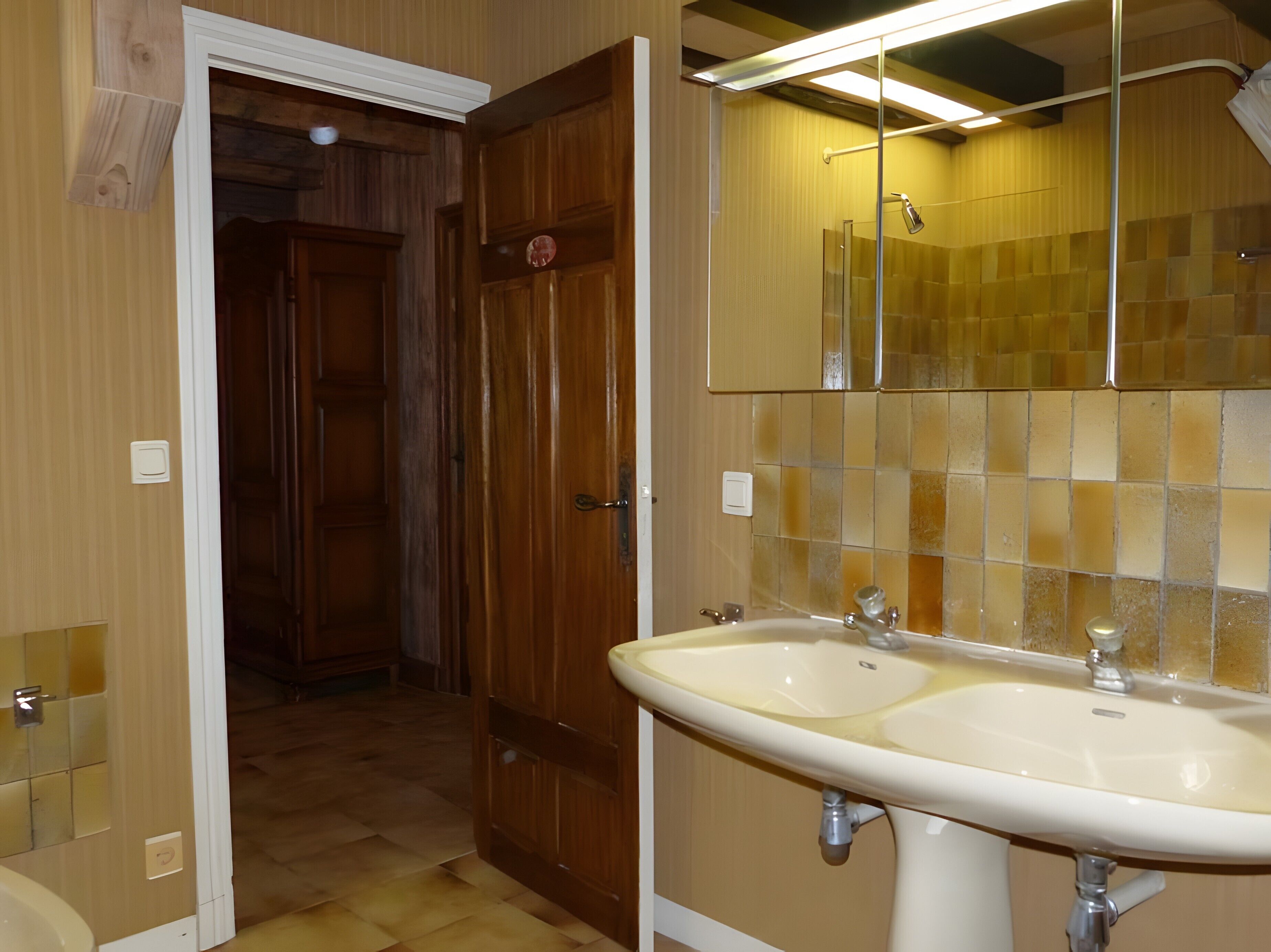 Un baño con puerta de madera, un lavabo doble y un espejo encima.