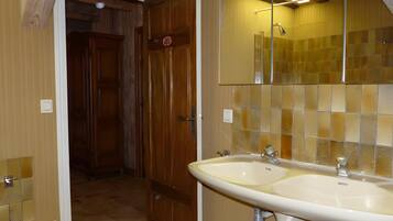 Un baño con puerta de madera, un lavabo doble y un espejo encima.