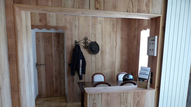 Interior de madera con una mesa, sillas, una puerta y un perchero en la pared.