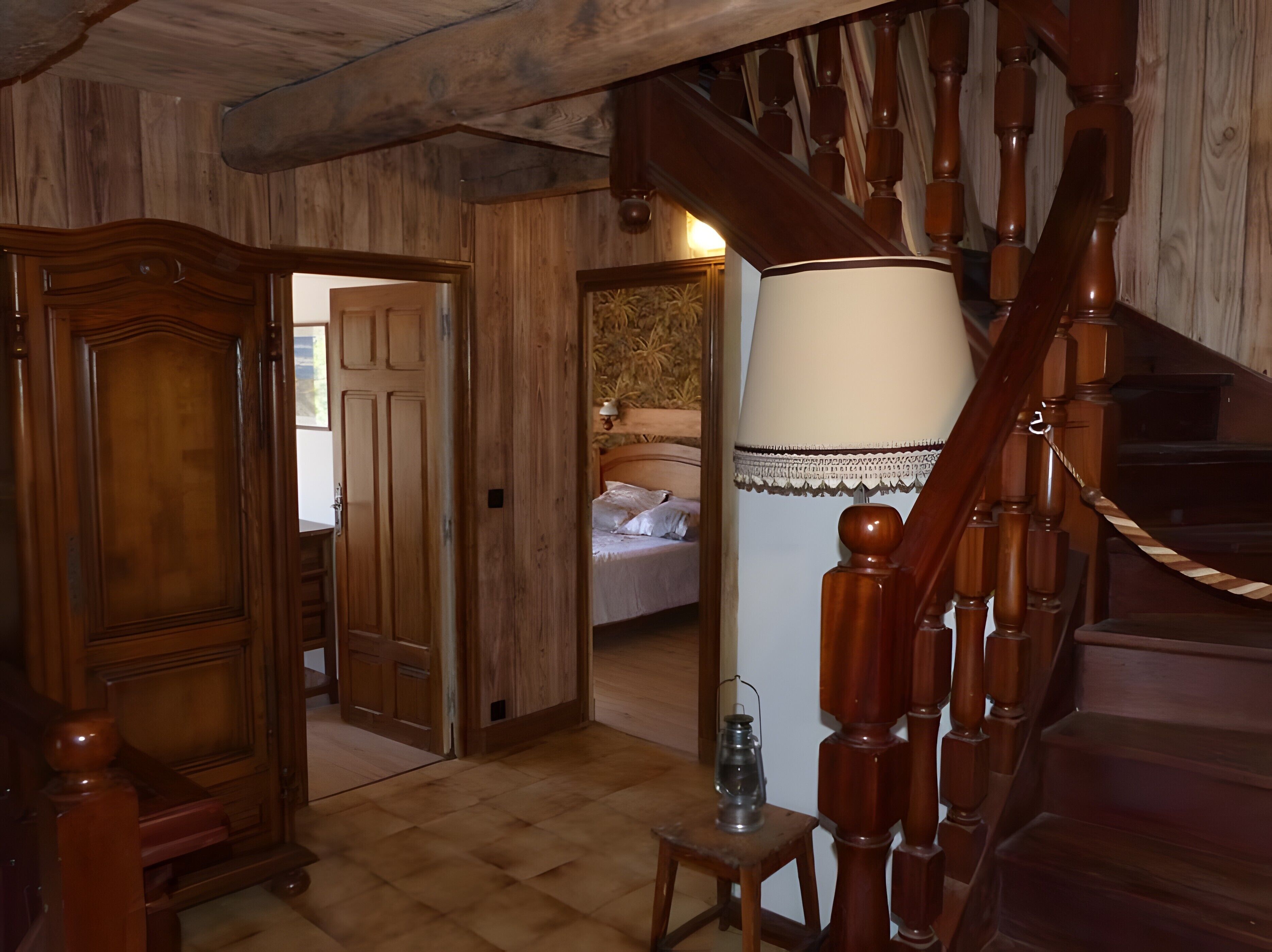 Un escalier en bois avec une rampe, un lit recouvert de draps blancs et une porte en bois donnant sur une autre pièce.