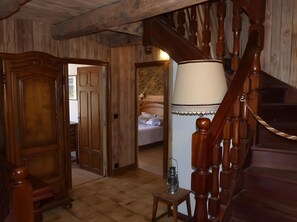Eine Holztreppe mit Handlauf, ein Bett mit weißen Leinen und eine Holztür, die in einen anderen Raum führt.