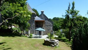 Una casa de piedra con chimenea de piedra, un espacio de estar al aire libre cubierto y un césped bien cuidado.