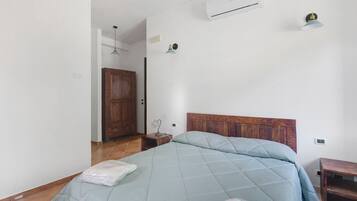 A bedroom with a bed, a wooden wardrobe, an air conditioning unit, and a nightstand with a lamp.