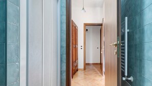 Un pasillo con puerta de madera, radiador metálico y lámpara colgante.