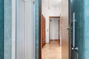 Un pasillo con puerta de madera, radiador metálico y lámpara colgante.
