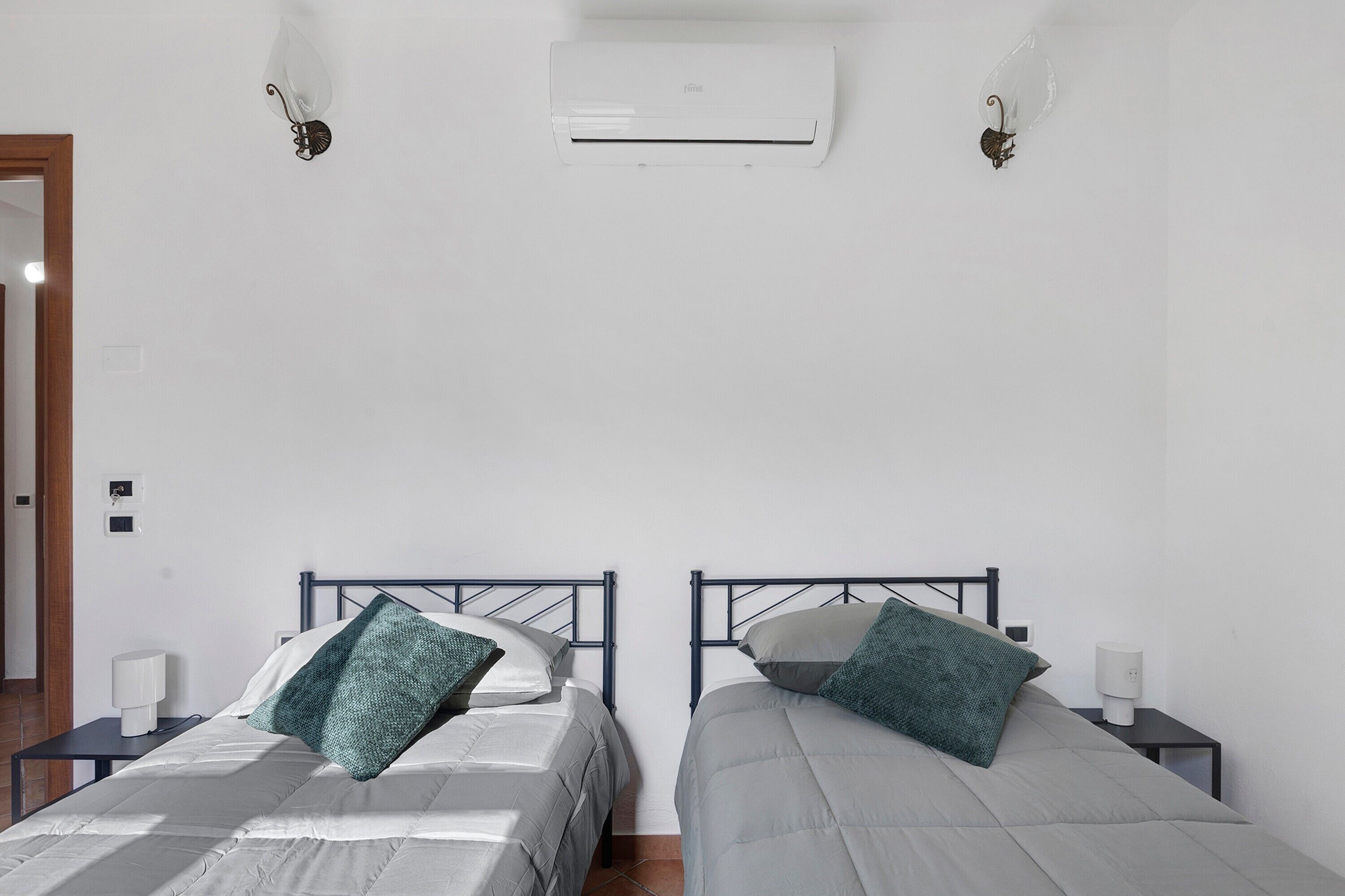 Une chambre avec deux lits, chacun étant équipé d’un oreiller et d’une table de chevet. Un appareil de climatisation est fixé au mur.