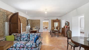 Uma sala de estar ampla com um sofá floral, uma mesa de jantar com cadeiras e uma parede de pedra.