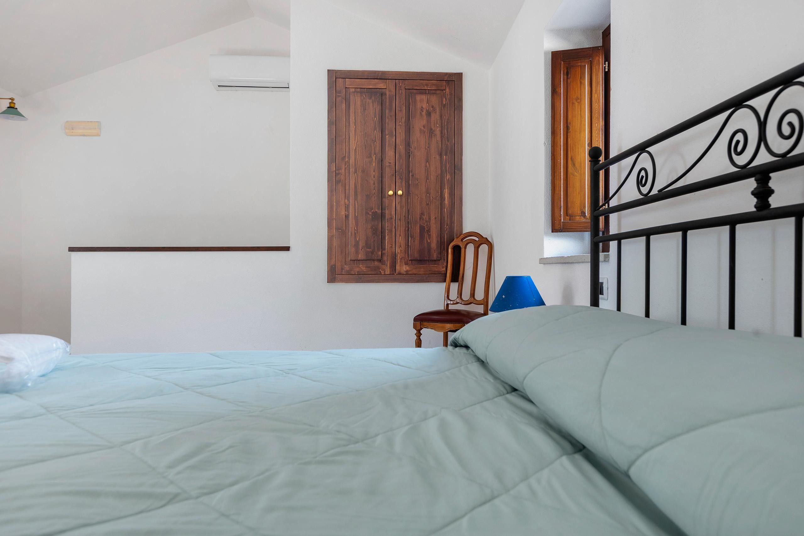Une chambre à coucher avec un lit, une armoire en bois, une chaise et une fenêtre.
