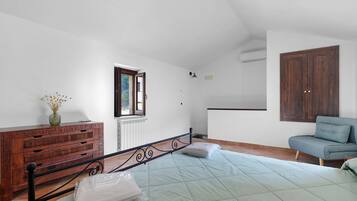 Une chambre à coucher avec un lit, une commode en bois, une fenêtre, un radiateur, un climatiseur mural et un canapé bleu.