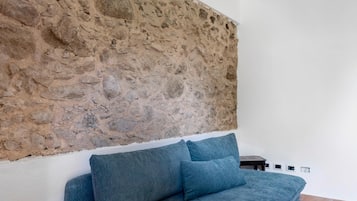A room with a stone wall, a bed with blue bedding, and a small table.
