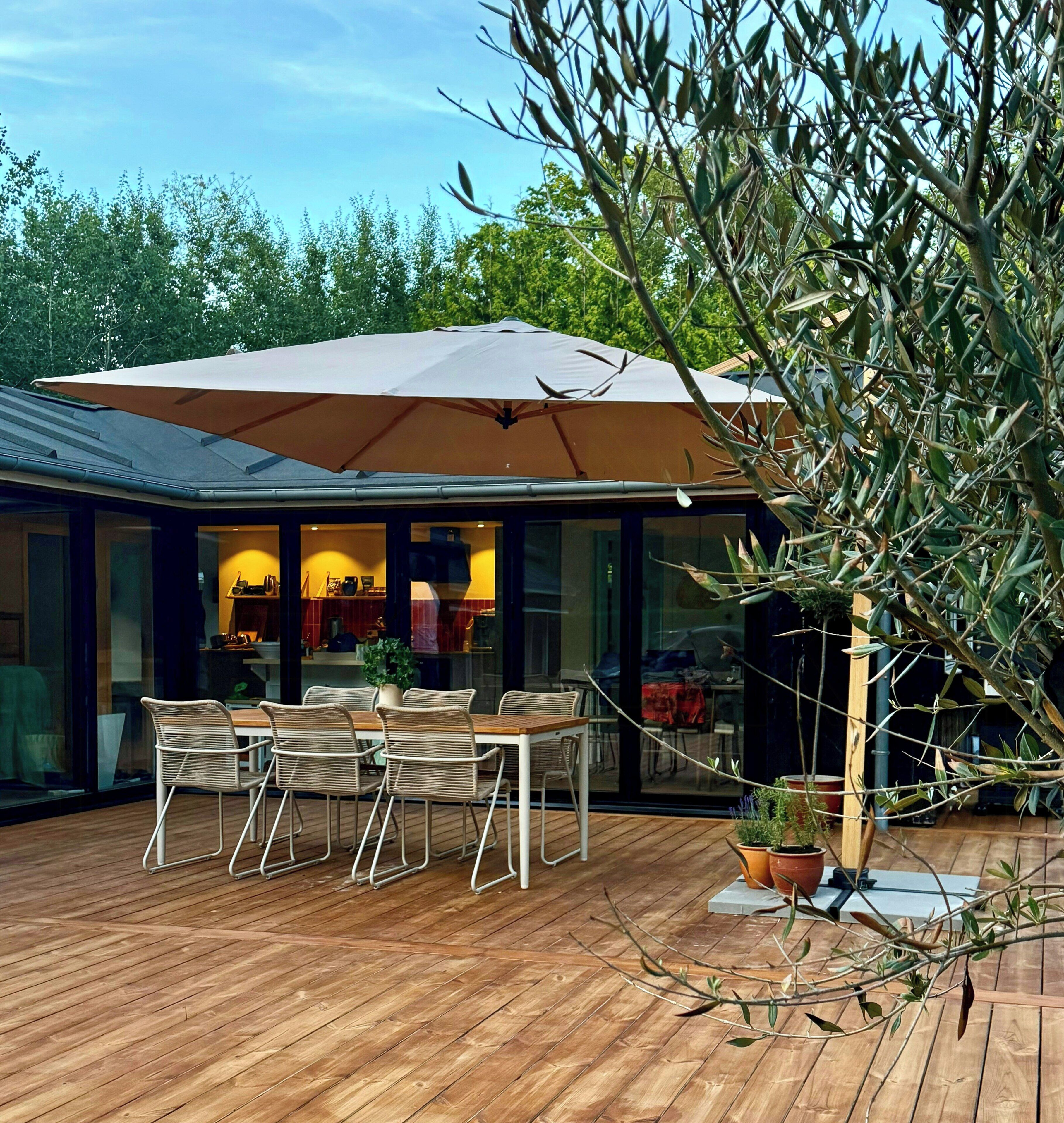 Een buiten eethoek met een tafel, stoelen, een grote parasol en een potplant.