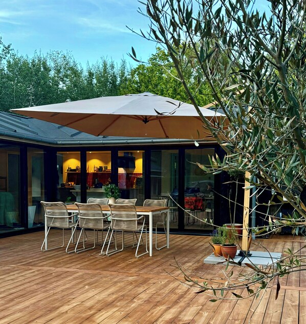 An outdoor dining area with a table and chairs, a large umbrella, and a potted plant.