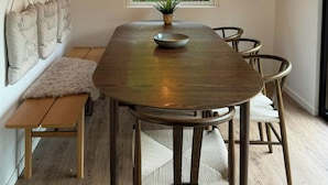 A dining area with a wooden table, chairs, a bench, a hanging lamp, and a window with a view of greenery.