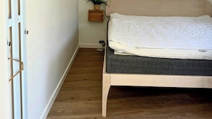 A bedroom with a bed, a hanging light fixture, a mirror, and a coat rack.