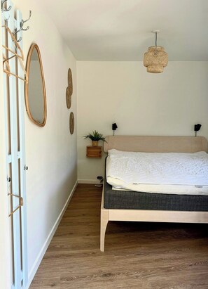 A bedroom with a bed, a hanging light fixture, a mirror, and a coat rack.