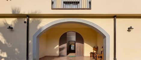A building with an arched entrance, a balcony with a window, and a door leading to an interior space.