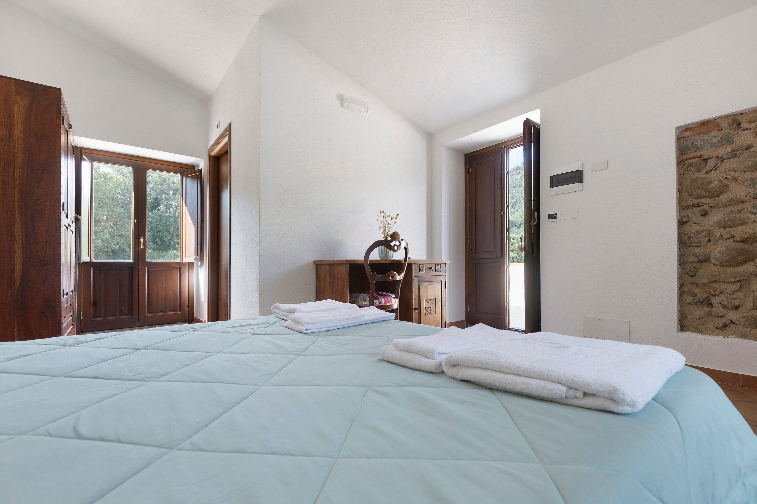 A bedroom with a large bed, a wooden dresser, and a stone wall.
