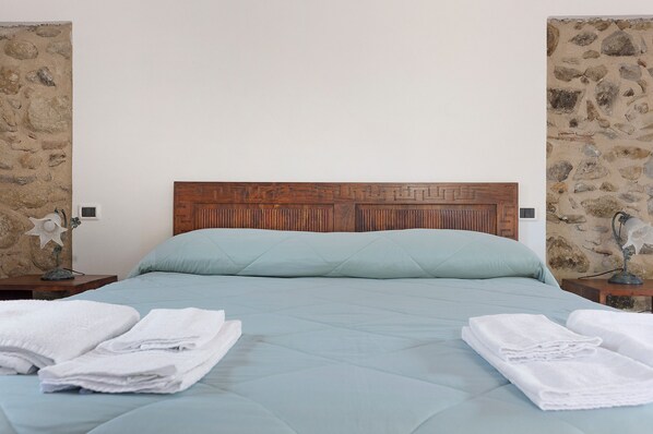 A bed with a wooden headboard, a light blue mattress, and two white towels on either side.