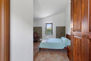 A bedroom with a bed, a chair, a window, and a view of the outdoors.