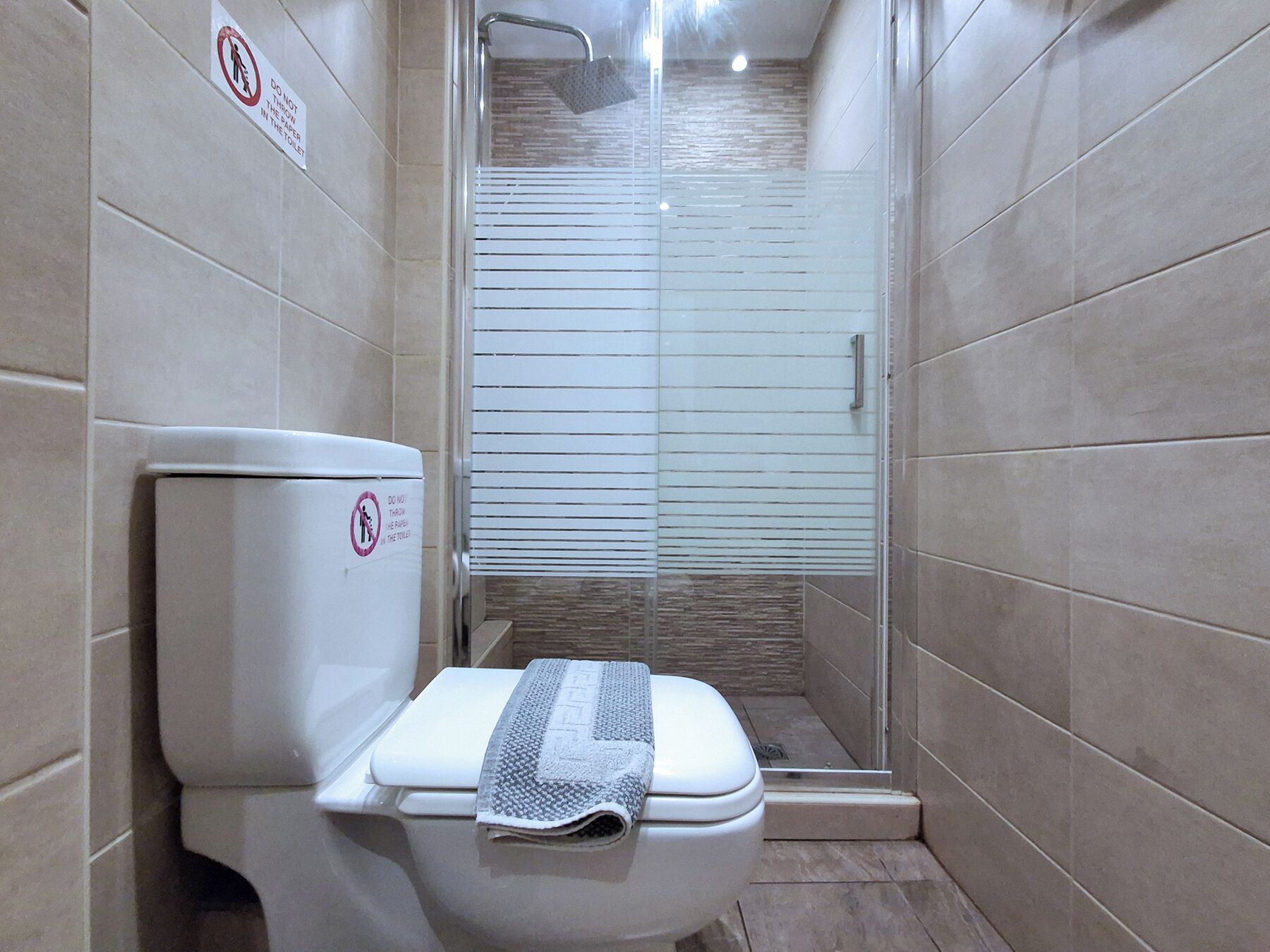 Un baño moderno con inodoro, cabina de ducha de vidrio y paredes de azulejos.