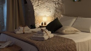 Ein Zimmer mit Steinsandsteinwand, einem Bett mit Kissen und Handtüchern, einem kleinen Tisch mit Lampe und einem Fenster mit Blick.