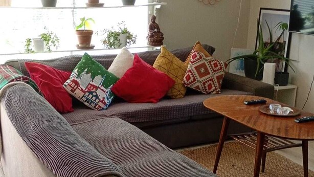 A modern living room with a sectional sofa, a coffee table, and a dining table. There are potted plants on a shelf and a Buddha statue on the wall. - Modern Cosy Townhouse in Laitila • Sauna, Terrace & Open-Plan Living (Laitila)