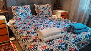 A bedroom with a bed, a nightstand, a lamp, a framed picture on the wall, and a patterned rug. - Modern Cosy Townhouse in Laitila • Sauna, Terrace & Open-Plan Living (Laitila)