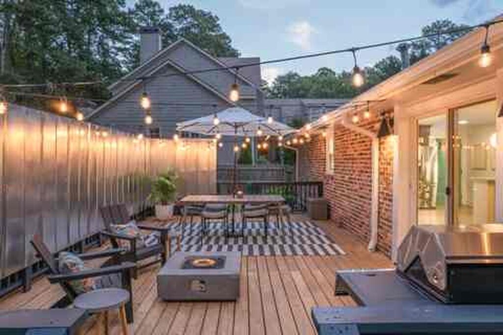 Um terraço com móveis de exterior, churrasqueira e luzes de corda.