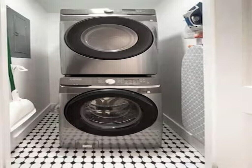 Een wasserette met een gestapelde wasmachine en droger, een betegelde vloer, en een magnetron aan de rechterkant.