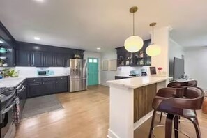 Una cocina moderna con armarios oscuros, una isla central con taburetes de bar, electrodomésticos de acero inoxidable e iluminación colgante.