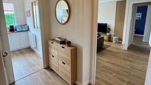 A spacious room with a wooden floor, a wooden cabinet, a round mirror, and a view into another room with a TV and a plant. - L'Escale Nippone – Wi-Fi – Free Parking (Vichy)