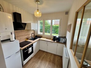 A modern kitchen with a black stove, white cabinets, a wooden countertop, and a window with a view of greenery. - L'Escale Nippone – Wi-Fi – Free Parking (Vichy)