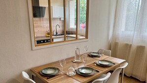 A dining area with a wooden table set for four, white chairs, and a large mirror above the table. - L'Escale Nippone – Wi-Fi – Free Parking (Vichy)