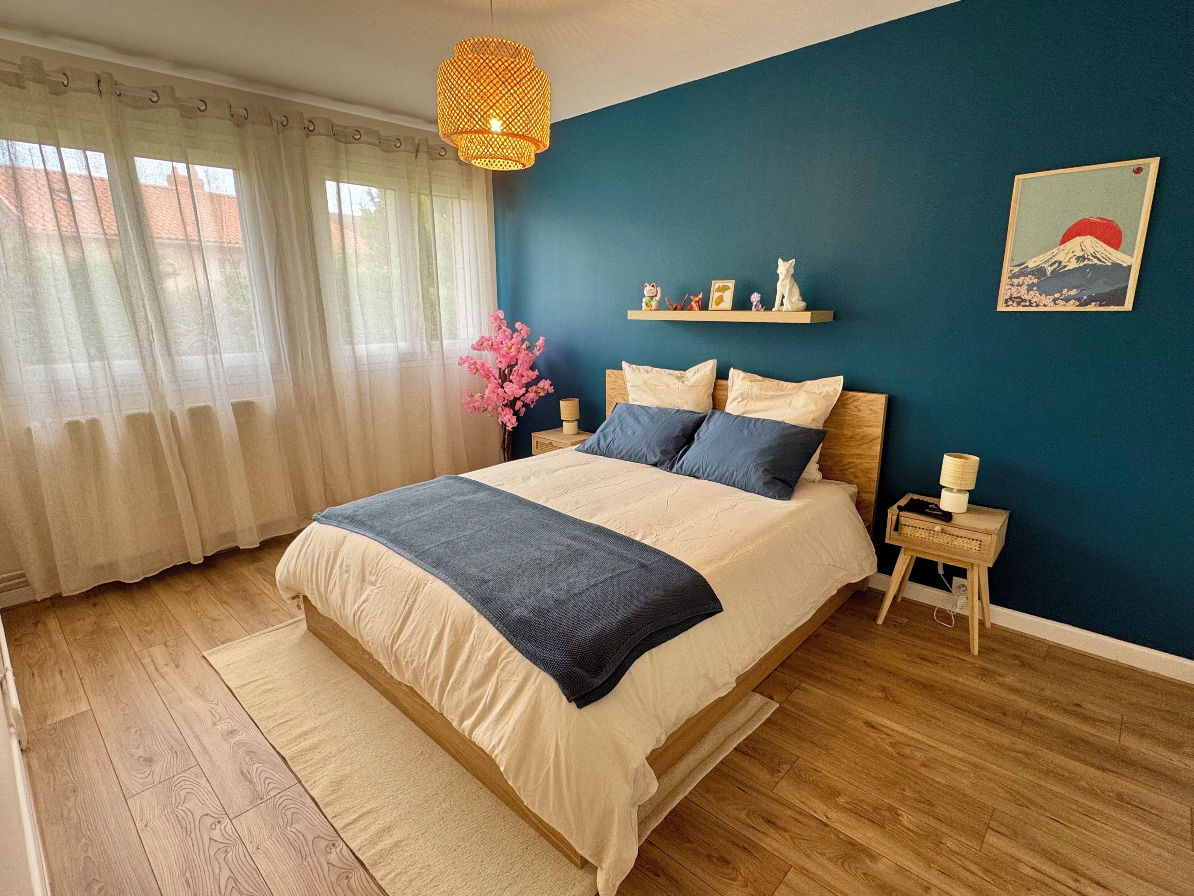 A bedroom with a bed, a nightstand, a lamp, a wall-mounted shelf with decorative items, and a painting.