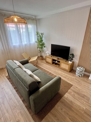 A modern living room with a sofa, television, and a bamboo plant. - L'Escale Nippone – Wi-Fi – Free Parking (Vichy)