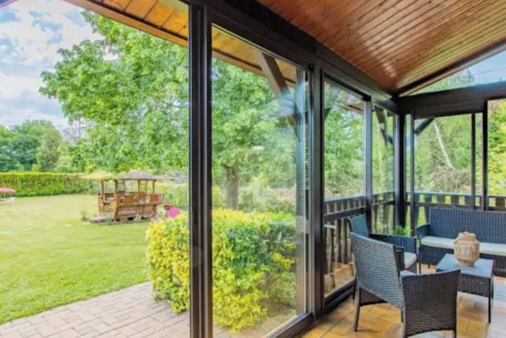 A covered outdoor seating area with a view of a garden and a gazebo.