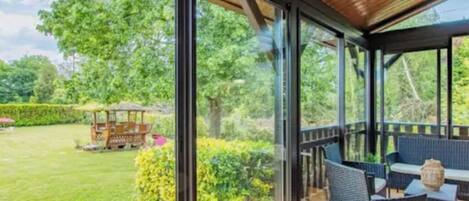 A covered outdoor seating area with a view of a garden and a gazebo.
