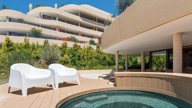 A modern building with a pool area, outdoor seating, and a view of a multi-story structure in the background. - Brinkmann | Modern - Plunge Pool - Terrace (Fuengirola)