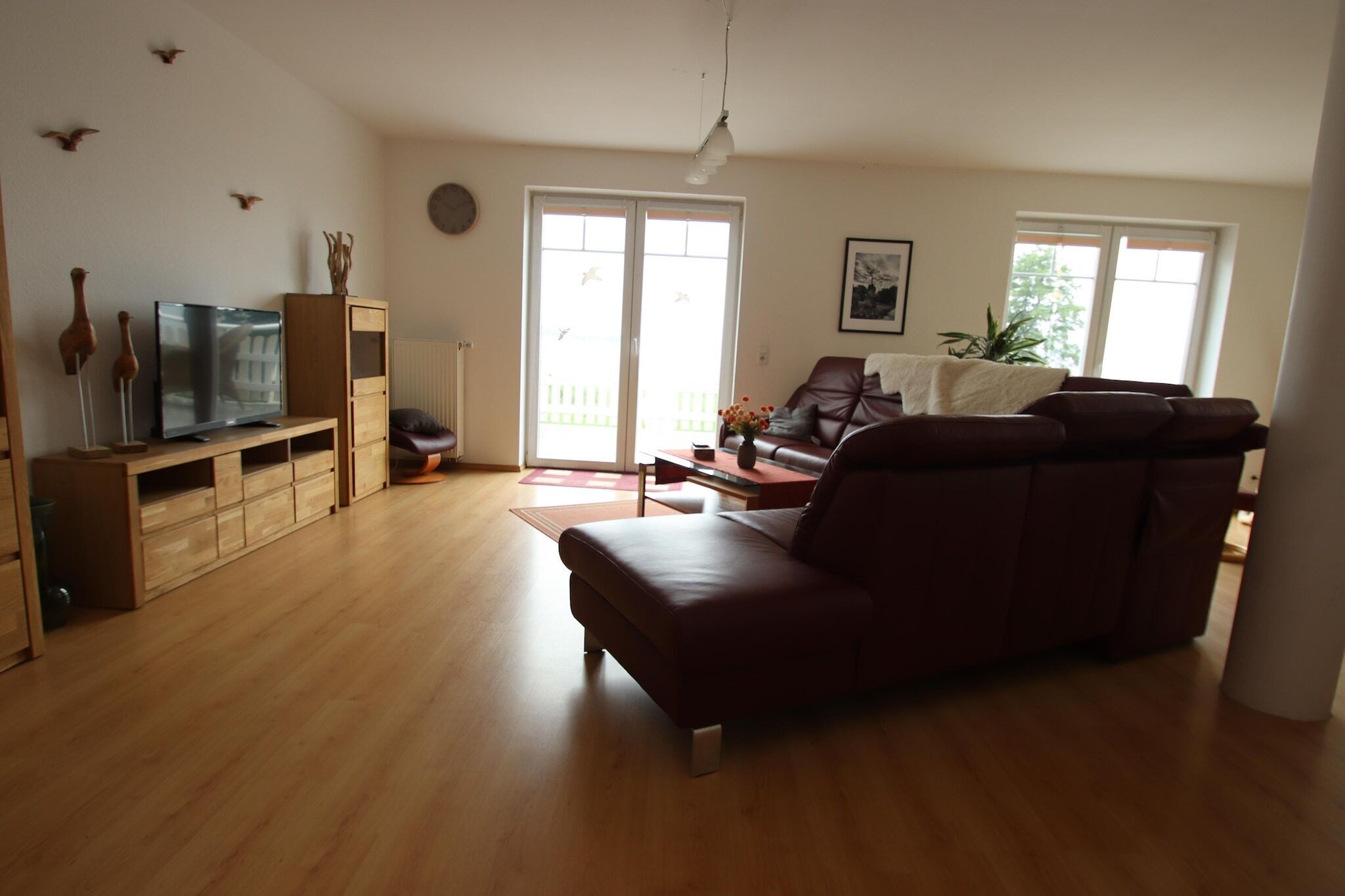 Un salon avec un canapé en cuir marron, des meubles en bois, un téléviseur et une porte-fenêtre coulissante donnant sur un balcon.