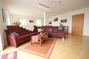 Uma sala de estar ampla, com um sofá vermelho, uma mesa de centro e piso de madeira.